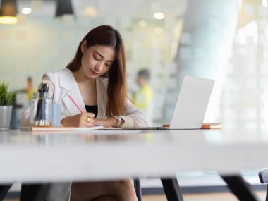 Laptop ve kırtasiyeyle işine odaklanan kadın ofis çalışanının portresi 