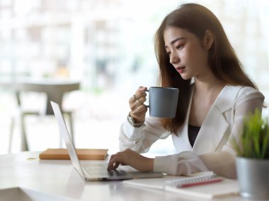Ofis odasında laptopla çalışırken kahve içen kadın ofis çalışanının portresi. 