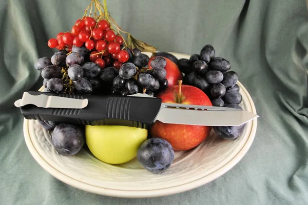 Folding knife stainless steel blade and fresh organic ripe fruits apples grape plums berries natural gourmet product dessert background