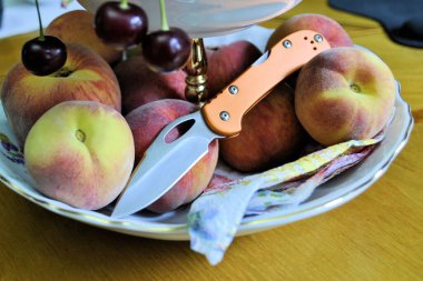 Katlanmış, paslanmaz çelik bıçaklı turuncu alüminyum saplı ve taze organik meyveli şeftalili, şeftalili, doğal gurme tatlı. Arka planda yakın plan.