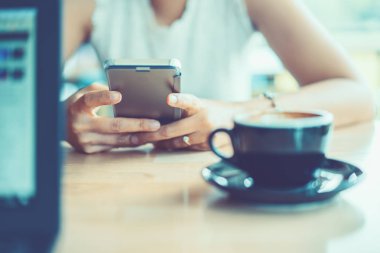 Dizüstü bilgisayar yeri üzerinde kahve ile akıllı telefon tutan kadın elleri o