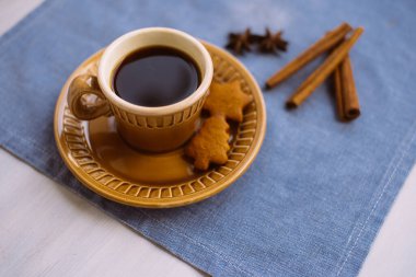 Bir fincan kahve ve lezzetli bir Noel kurabiyesi beyaz masadaki mavi keten peçetenin üzerinde yatıyor..