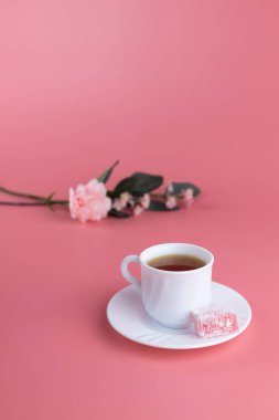 Beyaz bir fincan çay, yanında bir parça lokum, yanında Türk lokumu, pembe arka planda narin çiçekler. Öğleden sonra çay konsepti