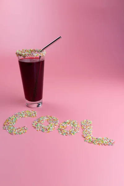 Word Cool written with colorful candy and a red drink, on a pink background, halloween concept