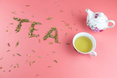 Bir fincan çay ve beyaz bir çaydanlık ve parlak pembe arka planda gevşek yaprak çayıyla yazılmış çay.