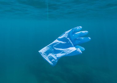 Akdeniz 'de yüzen mavi koruyucu eldiven kullanılmış. Katalonya, İspanya. Covid-19 kirliliği. Coronavirus önleme riskleri