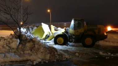 Kar temizleme aracının yan görüntüsü bir yığından kar topluyor geceleri onu taşımak için.