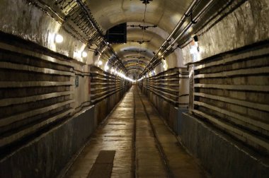 Geçen yüzyılın yeraltı askeri istihkamının kemerli tavanına sahip uçsuz bucaksız koridorda yerde tramvaylar, haberleşme ve elektrik kabloları, duvarlarda Ouvrage Schoenbourg, Maginot Hattı, Fransa - Temmuz 2017