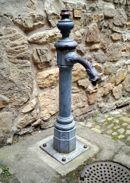 Old street public water pump against the stone wall