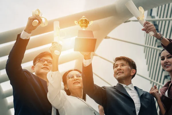 asyalı iş adamları kupa ve kazanan sertifika tutarak ellerini yükseltmek