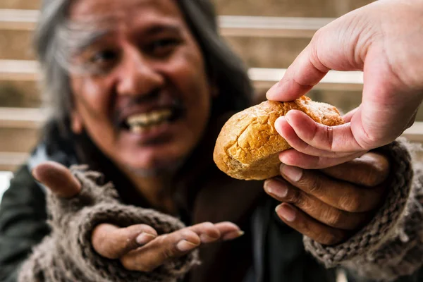 Рука дает хлеб или пищу размытому счастливому лицу бездомного мужчины — стоковое фото