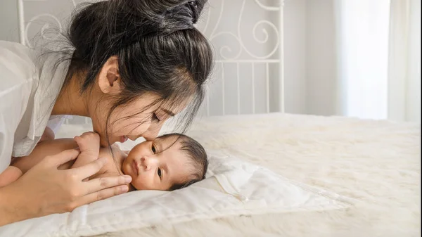 Asyalı anne tutan ve yatakta onu sevimli bebek erkek öpüşme — Stok fotoğraf