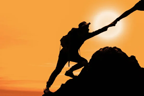 silhouette of man climbing up mountain with hand giving help