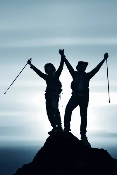 silhouette of two friends having achievement climbing up mountai