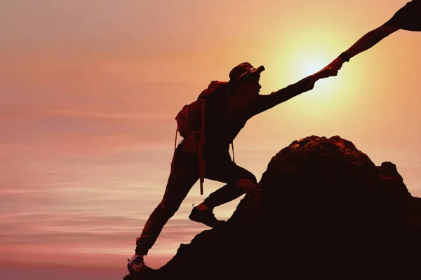 silhouette of man climbing up mountain with helping hand