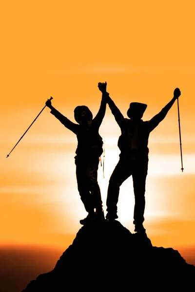 silhouette of two friends having achievement climbing up mountai