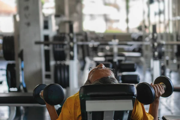 Senior masculino ejercitando levantando mancuernas en gimnasio — Foto de Stock