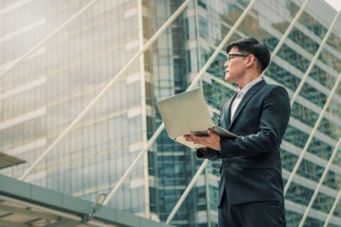 dizüstü bilgisayar kullanarak açık havada duran asyalı işadamı