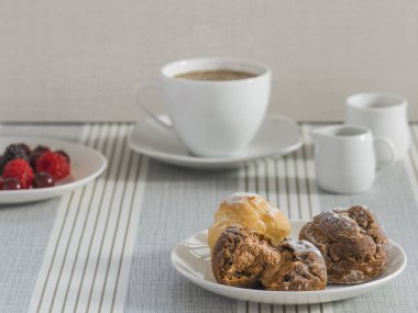 Bir fincan çay veya kahve ve v bir tabak ile chou krem bir tabak