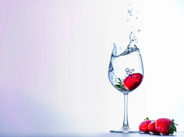 Fresh strawberry fall into a clear glass with water splashing an