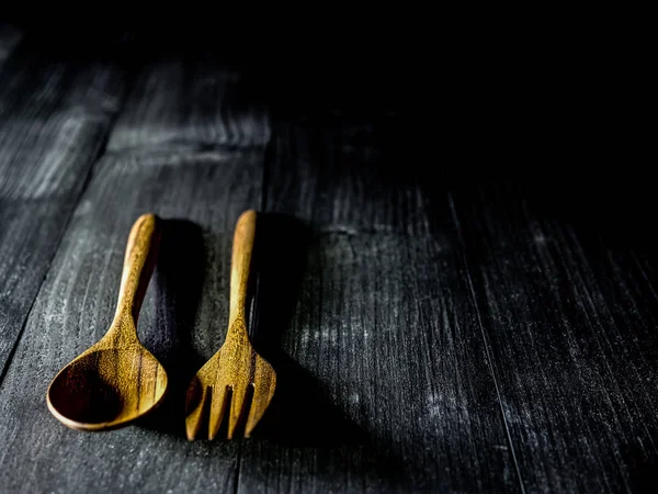 Cucchiaio e forchetta in legno su un tavolo di legno scuro con luce soffusa, sel — Foto Stock