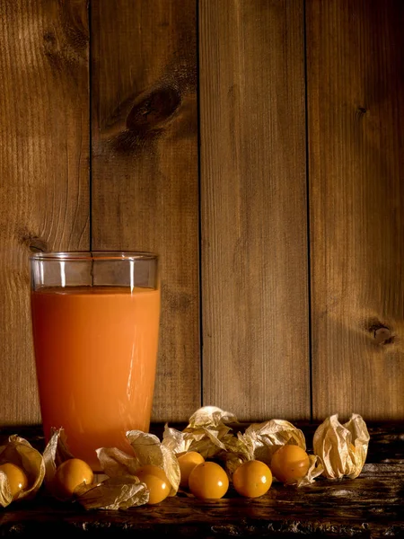 Grosellas del Cabo y un vaso de jugo de grosella del cabo sobre una madera — Foto de Stock