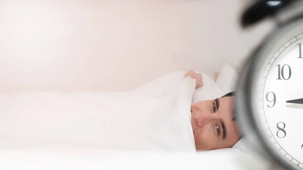 Alarm clock beside bed with background of wake up male in bed — Stock Photo, Image