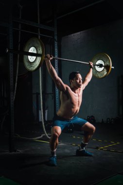 Asyalı güçlü adam spor salonunda ve spor salonunda ağırlık kaldırıyor.