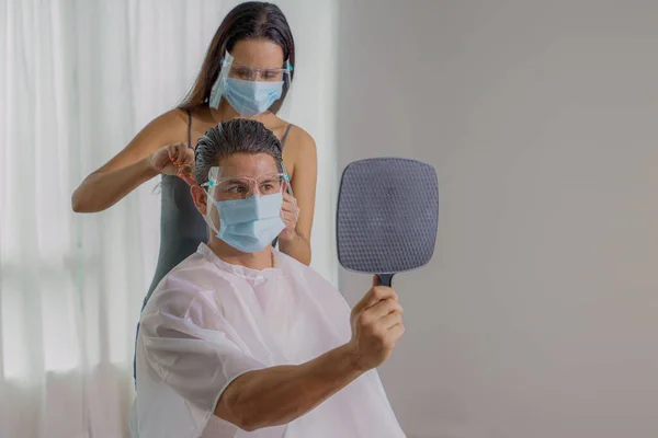 new normal practise caucasian man with face mask and face shield having haircut at hair salon by woman hairdresser wearing face mask and face sheild during coronavirus covid-19 pandemic