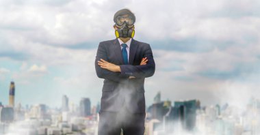 İş adamı kılığındaki iş adamı gaz maskesi takıp binanın çatısında dikiliyor. Şehrin arka planında bina ve gökdelenlerin dumanı ve kirli havayla kaplı.