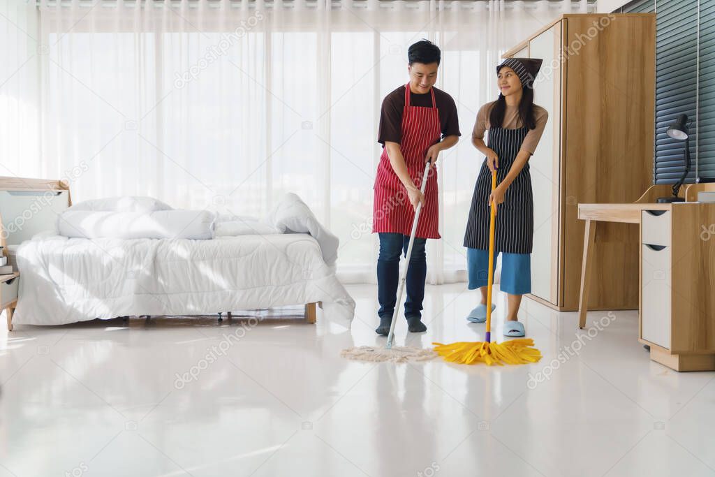 asian young couple having fun doing houseworks together. hasband and wife enjoy housecleaning using mop for floor cleening together