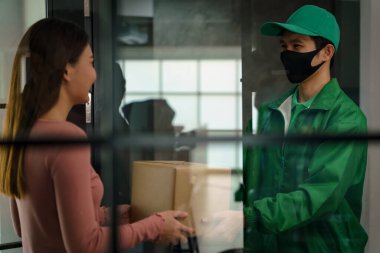 Yeşil üniformalı teslimatçı Coronavirus covid-19 'u korumak için maske takıyor.