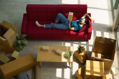 Kanepede uzanan Asyalı kadın evden taşınan mukavvaları açtıktan sonra oturma odasında dinleniyor.