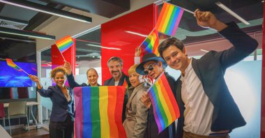 diverse group of business people (man, woman, gay, transgender, lesbian, asian, caucasian, african american, lgbtq) with rainbow flag on hand combine together as teamwork in office, selective focused clipart