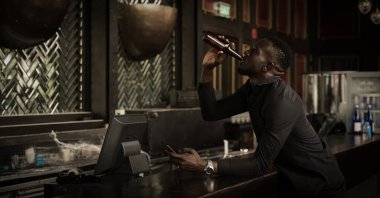 Afrikalı Amerikalı iş adamı rahatlayıp, bar ve kulüpte bir şişe bira içmenin tadını çıkarıyor.