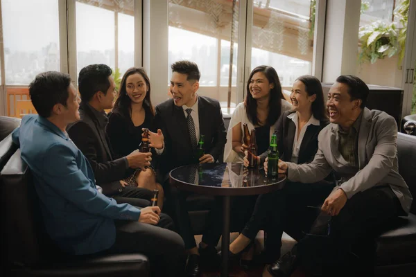 asian businesspeople clinking bottle of beer and talking together to celebrate friendship in business lounge and club