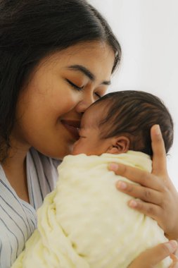 Afrika kökenli Afro-Amerikan ve Asyalı anne yeni doğmuş bebeğini mutlu yüzüyle nazikçe öpüyor.