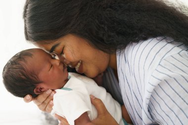 Karışık ırk Afro-Amerikan ve Asyalı anne yeni doğmuş bebeğini mutlu bir suratla tutuyor.