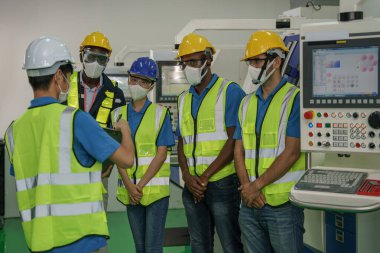 Fabrika işçilerinin ve yüz maskesi takan teknisyenlerin güvenlik yeleği ve miğferi ile Coronavirus covid-19 'u korumak için güvenlik yeleği ve miğferi olan endüstri geçmişi kontrol odasındaki fabrika ustabaşısından çalışma detayları alıyor.