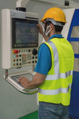 CNC makine kontrol panelinde çalışan Coronavirus covid-19 'u korumak için güvenlik yeleği ve kasklı beyaz fabrika işçisinin portresi.