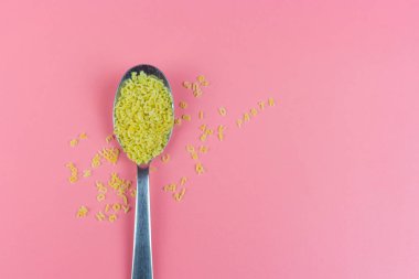 Pembe arka plan üzerinde gümüş kaşık alfabe makarna  