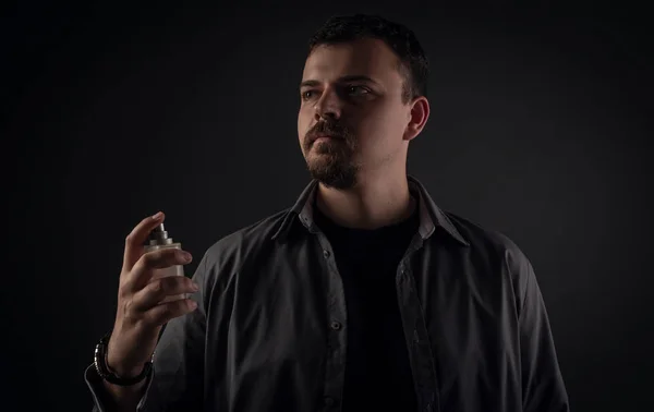 bearded man with perfume on a dark background