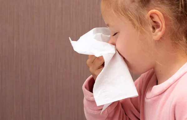 child girl has runny nose and blows her nose into a tissue paper