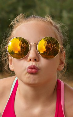 Güneşli bir günde, güneş gözlüklü, gülümseyen küçük kız.