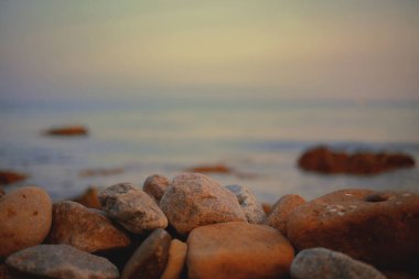 Sahildeki çakıl taşları, arka plandaki bulanık gün batımı ışığında yakındır..