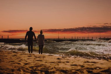 Gün batımında sahilde gezinen bir çift.