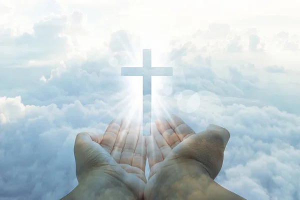 Hands cupped with a shining white cross hovering above on a sunn — Stock Photo, Image