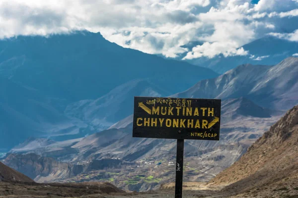 Black pointer to the fork in the road in Muktinath and Chhyonkhar on a background of mountains and clouds, Nepal.