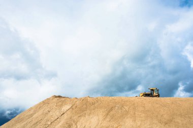 Kum bulutlu gökyüzü arka plan üzerinde büyük bir tepe üzerinde sarı buldozer.