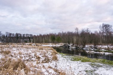 Sonbahar bir bulutlu gün sarı kuru ot küçük bir nehir kıyısında ilk beyaz kar düştü. 